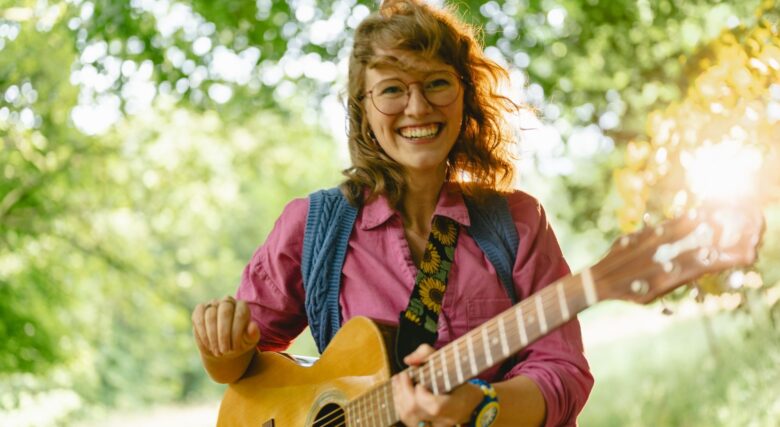 Singer-songwriter Jessica smiling playing her guitar.
