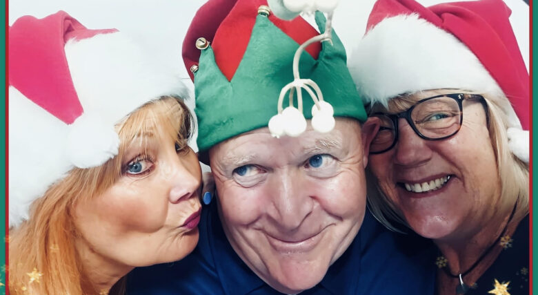 Three performers smiling wearing Christmas hats